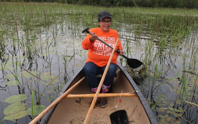 Woman paddling a canoe to harvest wild rice. 