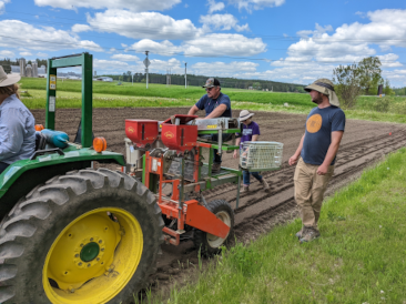 Program members on and near a tractor planter that is planting a row in a paddy.